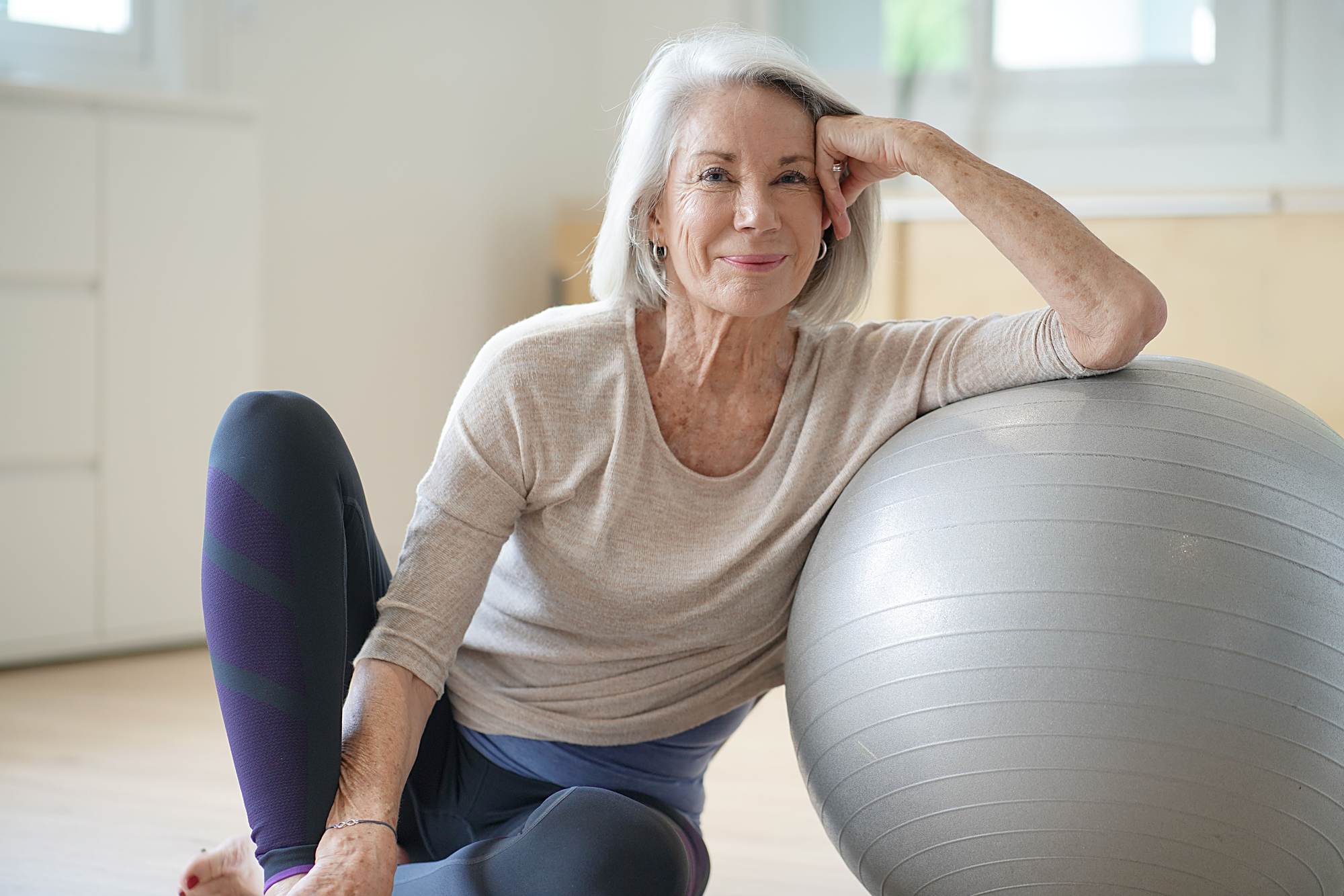 Smiling senior woman sitting on the floor with an exercise ball